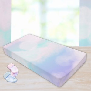 Könnte beinhalten: Ein pastellfarbenes, blau, rosa und grünes, gemustertes Spannbettlaken für ein Babybett. Das Laken ist aus weichem, atmungsaktivem Stoff und perfekt für ein Babyzimmer.