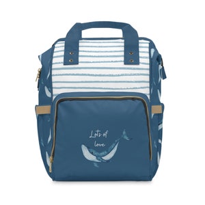 以下が含まれることがあります： 青と白のストライプのオムツバッグ。クジラのデザインと「Lots of love」の文字が入っています。