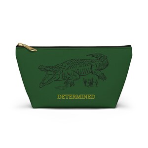 May include: A green zippered pouch with a black line drawing of an alligator with the word "DETERMINED" in yellow text.