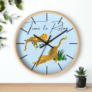 May include: A light blue round wall clock with black clock hands and black Roman numeral markings. The clock face features the text "Time to Relax" and two stylized leopard illustrations.