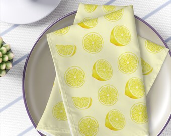Puede incluir: Dos servilletas de lino amarillas con estampado de limón. Los limones son amarillos sobre fondo blanco. Las servilletas están dobladas por la mitad y colocadas en un plato marrón claro con un borde morado.