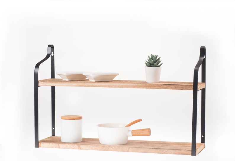 Puede incluir: Una estanter&iacute;a de madera de dos niveles con soportes de metal negro. La estanter&iacute;a est&aacute; decorada con platos blancos, una peque&ntilde;a suculenta en maceta, un tarro de cer&aacute;mica blanca con tapa de madera y una olla de cer&aacute;mica blanca con asa de madera.