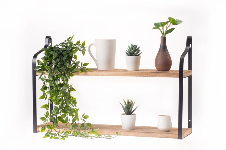 Puede incluir: Una estanter&iacute;a de madera de dos niveles con soportes de metal negro. La repisa superior tiene una taza blanca, una peque&ntilde;a suculenta en maceta y un jarr&oacute;n marr&oacute;n con hojas verdes. La repisa inferior tiene una peque&ntilde;a suculenta en maceta y una jarra blanca.