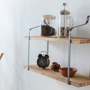 Puede incluir: Estanter&iacute;a de madera de dos niveles con soportes met&aacute;licos. La repisa superior tiene un frasco de vidrio lleno de granos de caf&eacute; y una prensa francesa de vidrio. La repisa inferior tiene un reloj despertador negro, una pi&ntilde;a y un taz&oacute;n de terracota.