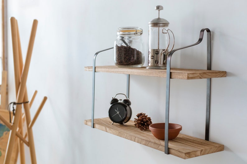Puede incluir: Estanter&iacute;a de madera de dos niveles con soportes met&aacute;licos. La repisa superior tiene un frasco de vidrio lleno de granos de caf&eacute; y una prensa francesa de vidrio. La repisa inferior tiene un reloj despertador negro, una pi&ntilde;a y un taz&oacute;n de terracota.