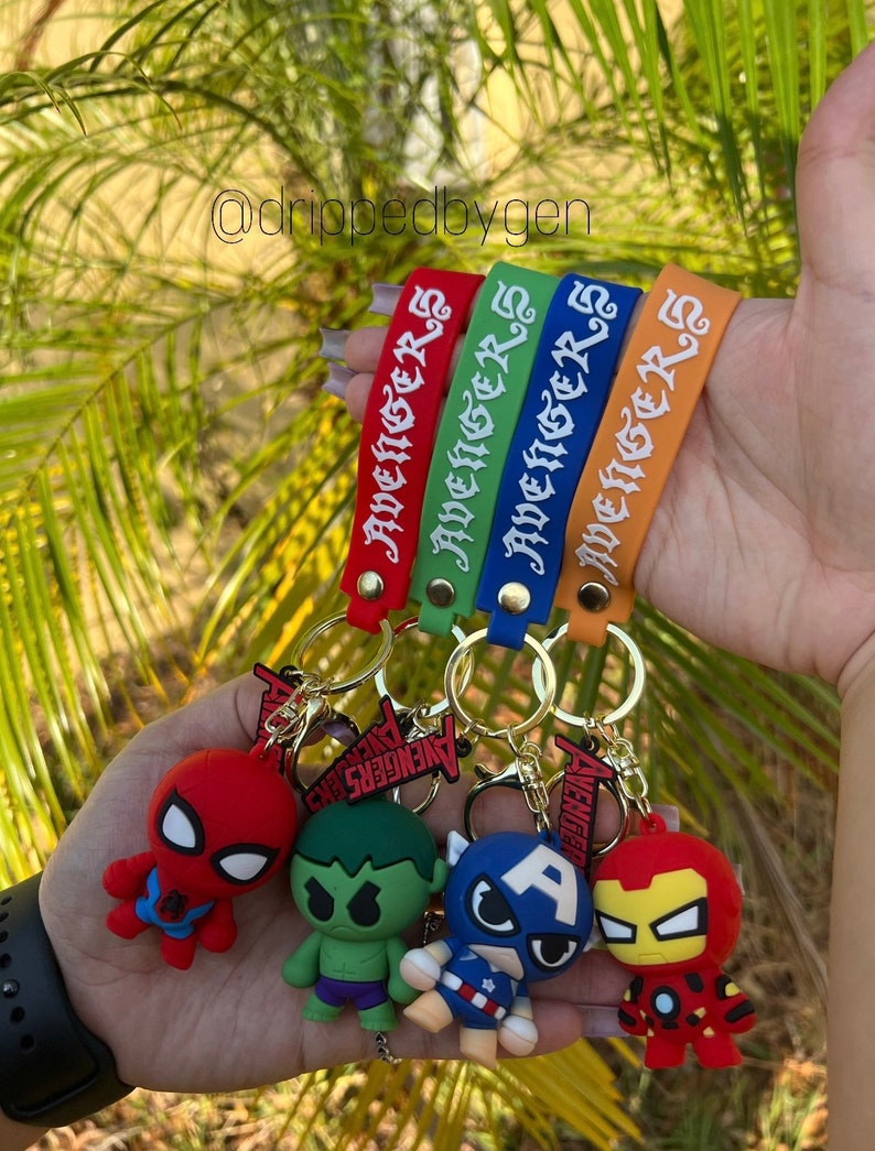 Op de afbeelding: Vier kleurrijke sleutelhangers met het woord "Avengers" erop. Elke sleutelhanger heeft een ander Avenger-personage: Spider-Man, Hulk, Captain America en Iron Man.