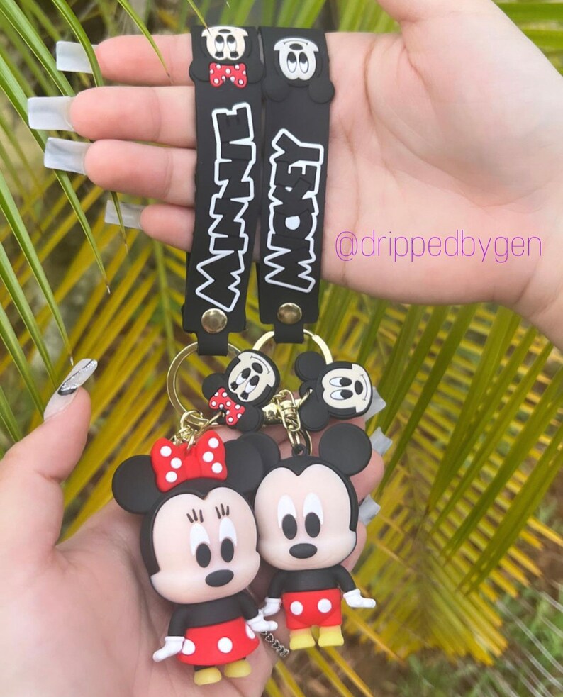 Op de afbeelding: Zwart-witte Mickey Mouse en Minnie Mouse sleutelhanger met rode accenten. De sleutelhanger heeft de woorden "Mickey" en "Minnie" op de bandjes.