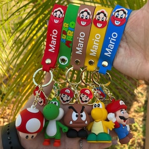 Op de afbeelding: Vijf kleurrijke siliconen sleutelhangers met verschillende Super Mario-personages. De sleutelhangers hebben de namen "Mario" en "Super Mario" in witte tekst. De personages zijn Mario, Luigi, Yoshi, Toad en Bowser.