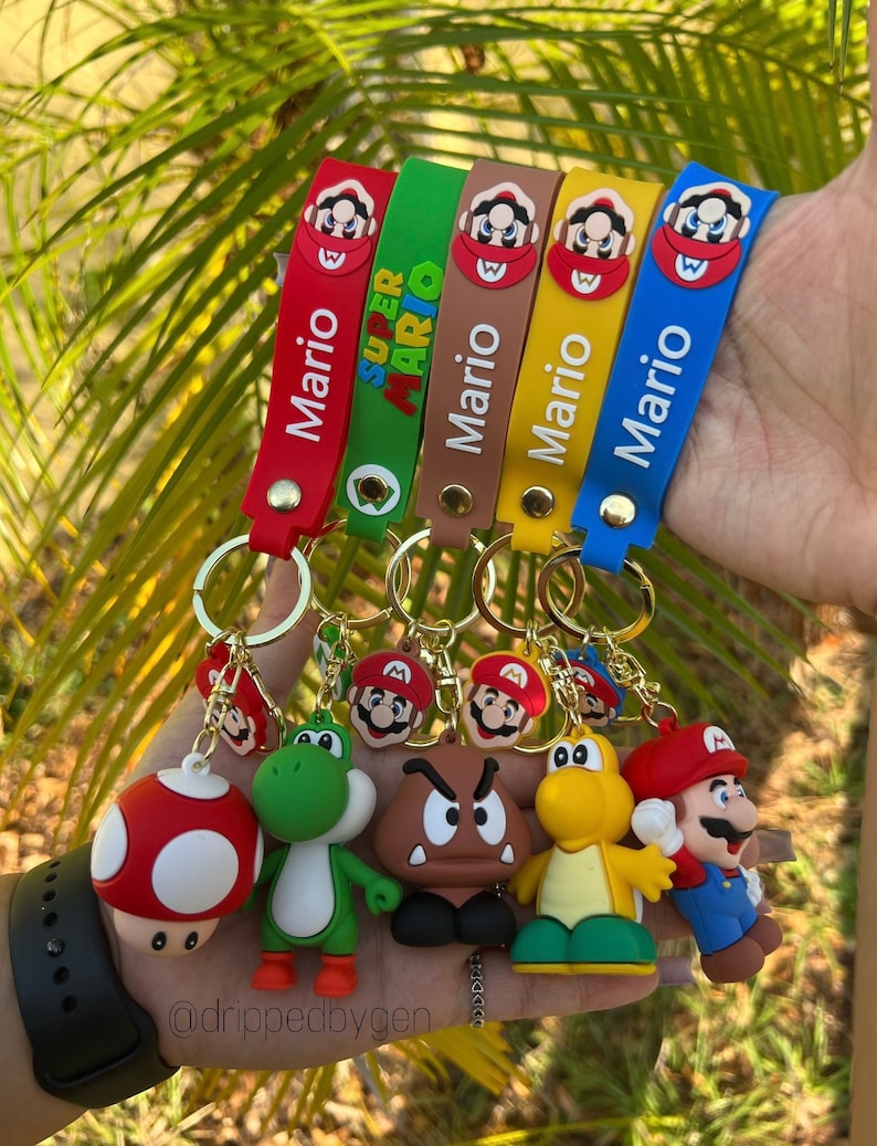 Op de afbeelding: Vijf kleurrijke siliconen sleutelhangers met verschillende Super Mario-personages. De sleutelhangers hebben de namen "Mario" en "Super Mario" in witte tekst. De personages zijn Mario, Luigi, Yoshi, Toad en Bowser.
