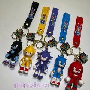 Op de afbeelding: Set van zes sleutelhangers met Sonic the Hedgehog-personages. Elke sleutelhanger heeft een ander personage uit de Sonic Heroes-videogame: Shadow, Super Sonic, Knuckles, Sonic en Rouge. Elke sleutelhanger heeft een gouden ring en een zwarte, gele, paarse, blauwe of rode band met het Sonic Heroes-logo.