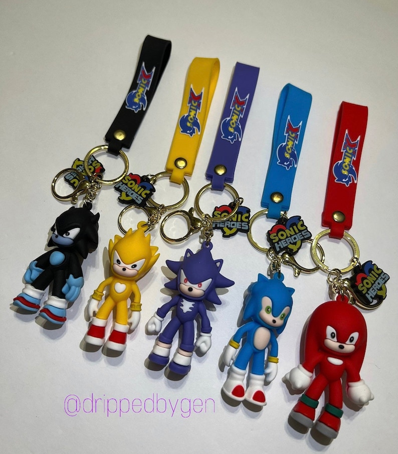 Op de afbeelding: Set van zes sleutelhangers met Sonic the Hedgehog-personages. Elke sleutelhanger heeft een ander personage uit de Sonic Heroes-videogame: Shadow, Super Sonic, Knuckles, Sonic en Rouge. Elke sleutelhanger heeft een gouden ring en een zwarte, gele, paarse, blauwe of rode band met het Sonic Heroes-logo.