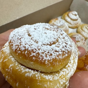 May include: A close-up of a sweet roll, dusted with powdered sugar. The roll is made of a soft, golden dough and has a slightly sweet, buttery flavor.