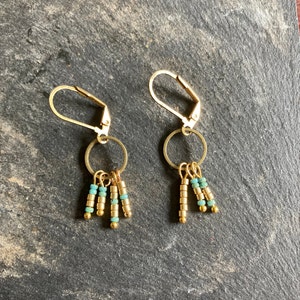 Puede incluir: Pendientes de aro dorados con colgantes de cuentas turquesa y doradas.