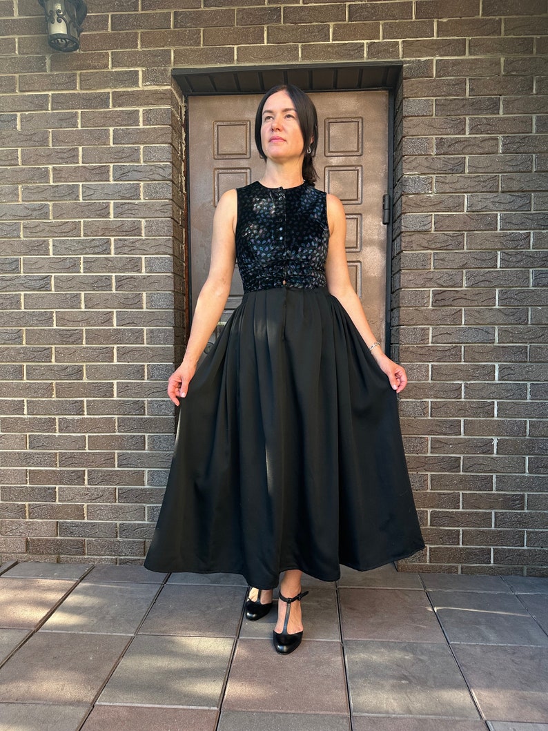 May include: A black sleeveless dress with a patterned bodice and a full skirt. The dress is worn with black heels.
