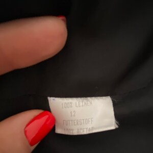 Puede incluir: Etiqueta blanca con texto negro que dice "100% Leinen 12 Futterstoff 100% Acetat"