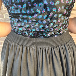 May include: A black skirt with a gathered waistband and a paisley print top. The top is made of velvet and has a blue, green, and pink paisley pattern.