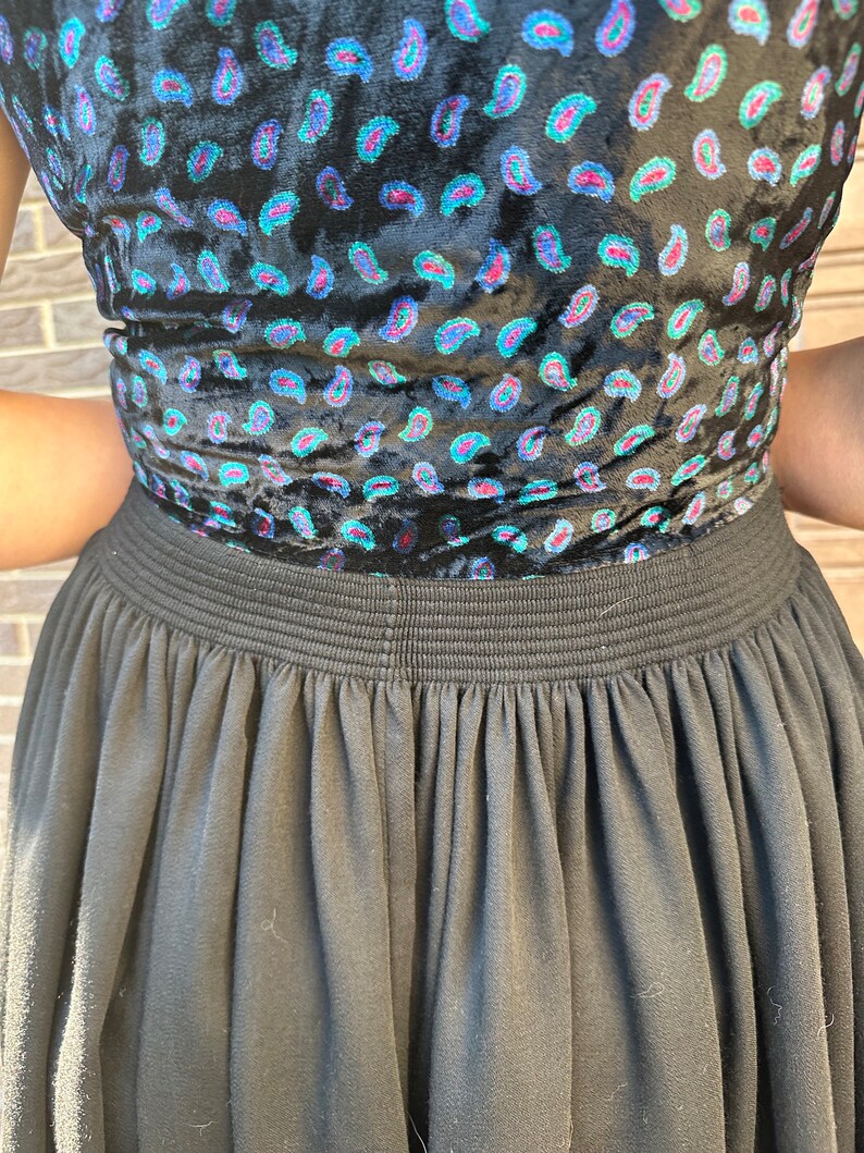 May include: A black skirt with a gathered waistband and a paisley print top. The top is made of velvet and has a blue, green, and pink paisley pattern.