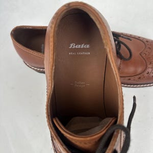May include: Brown leather dress shoes with decorative perforations and laces. The interior of the shoe is visible, displaying the brand "Bata" and the text "Real Leather". The words "Italian Design" are also visible.