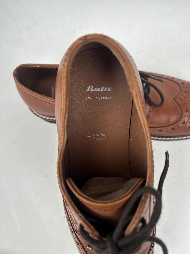 May include: Brown leather dress shoes with decorative perforations and laces. The interior of the shoe is visible, displaying the brand "Bata" and the text "Real Leather". The words "Italian Design" are also visible.