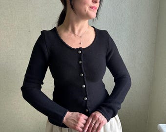 May include: A black knitted cardigan with a scoop neck and button fastening. The cardigan has long sleeves and a fitted silhouette.