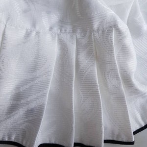 May include: White skirt with a black trim around the bottom. The skirt has a pleated design and a subtle floral pattern.