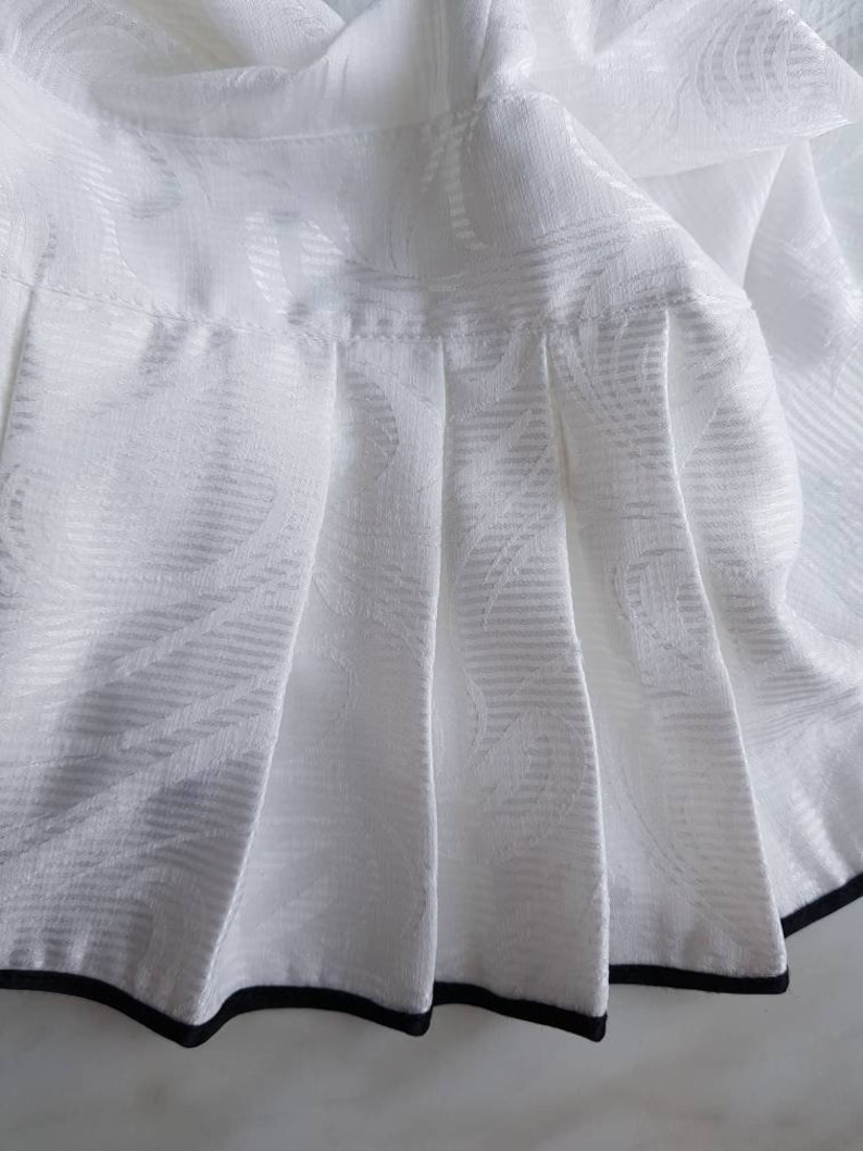 May include: White skirt with a black trim around the bottom. The skirt has a pleated design and a subtle floral pattern.