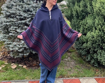 Puede incluir: Un poncho azul marino con capucha y un patrón geométrico burdeos y dorado. El poncho tiene un cierre de botón en el cuello.