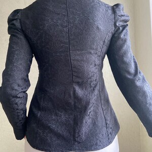 May include: Black long-sleeved blouse with a fitted silhouette and a subtle floral pattern. The blouse has a round neckline and a zipper closure in the back.