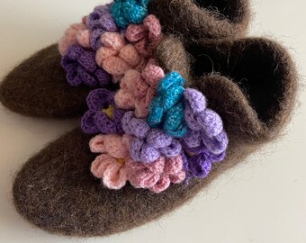 May include: A pair of brown wool slippers with a colorful crocheted flower design. The flowers are in shades of pink, purple, blue, and teal.