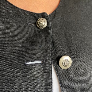 Puede incluir: Una chaqueta de lino negra con dos botones plateados. Los botones tienen un dise&ntilde;o floral decorativo.