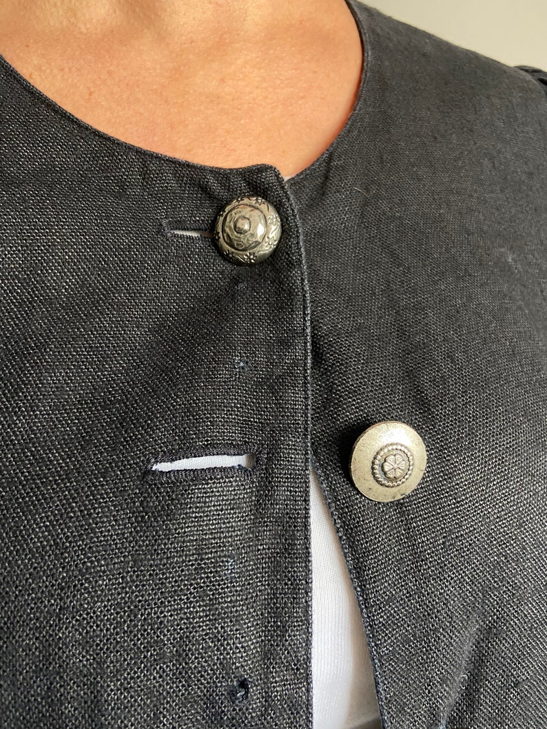 Puede incluir: Una chaqueta de lino negra con dos botones plateados. Los botones tienen un dise&ntilde;o floral decorativo.