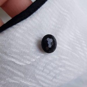May include: A close-up of a black, faceted button on a white fabric background.