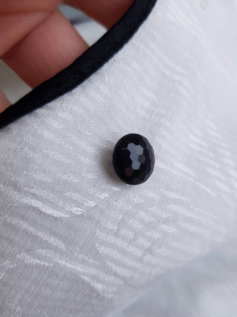 May include: A close-up of a black, faceted button on a white fabric background.