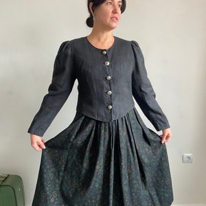 Puede incluir: Una chaqueta negra de lino con mangas abullonadas y botones plateados, puesta sobre una falda negra con estampado paisley verde y azul.