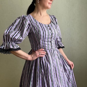 Puede incluir: Un vestido de rayas moradas y negras con un corpiño ajustado y una falda completa. El vestido tiene un escote redondo y mangas cortas con ribetes de encaje.