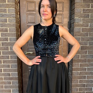 May include: A black sleeveless top with a floral pattern and a button-up front. The top is paired with a black skirt.