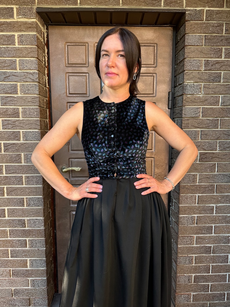May include: A black sleeveless top with a floral pattern and a button-up front. The top is paired with a black skirt.