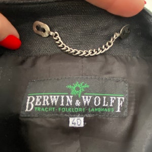 Puede incluir: Una chaqueta negra con una cadena plateada y una etiqueta que dice "Berwin & Wolff Tracht - Folklore Landhaus" con la talla "40" impresa debajo.