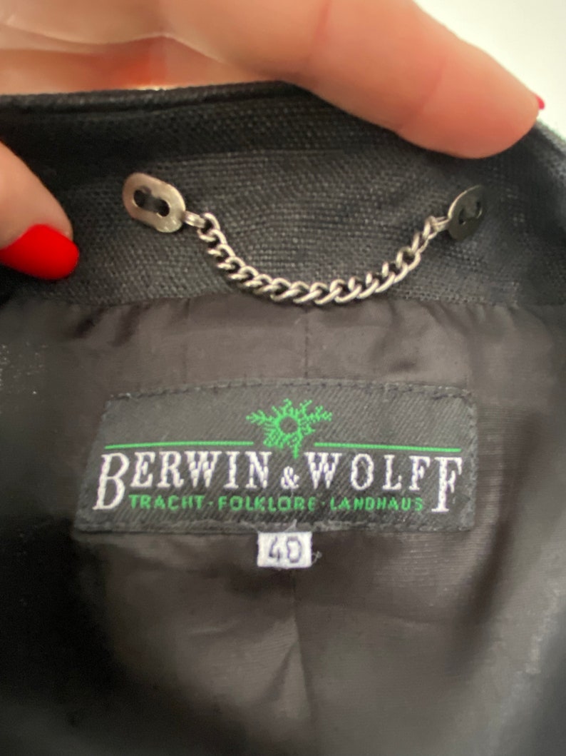 Puede incluir: Una chaqueta negra con una cadena plateada y una etiqueta que dice "Berwin & Wolff Tracht - Folklore Landhaus" con la talla "40" impresa debajo.
