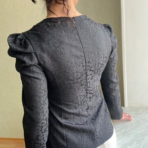 May include: Black long-sleeved blouse with a floral pattern and puffed sleeves.