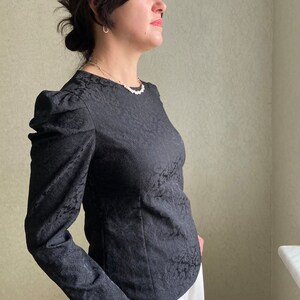 May include: A black long-sleeved blouse with a floral pattern and puffed sleeves.