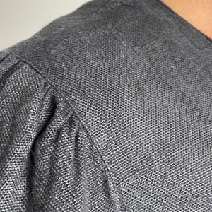 Puede incluir: Primer plano de una camisa de lino gris oscuro con tejido texturizado. La tela es suave y tiene un brillo sutil.