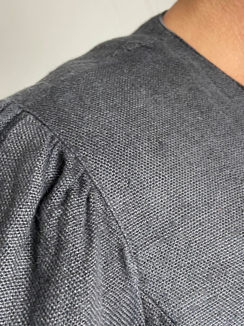 Puede incluir: Primer plano de una camisa de lino gris oscuro con tejido texturizado. La tela es suave y tiene un brillo sutil.