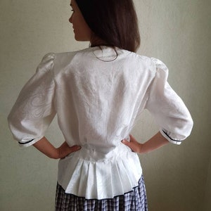 May include: White blouse with a ruffled hem and black trim. The blouse has a fitted bodice and 3/4 sleeves. The model is wearing a plaid skirt.