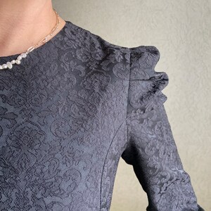 May include: A black dress with a floral pattern and puffed sleeves. The dress has a fitted bodice and a flowing skirt.
