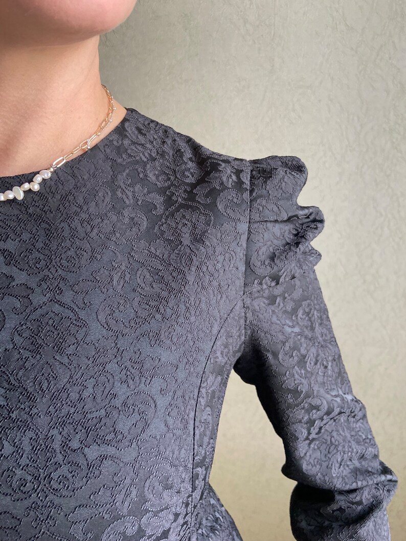 May include: A black dress with a floral pattern and puffed sleeves. The dress has a fitted bodice and a flowing skirt.