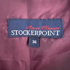 Puede incluir: Un interior de prenda de color morado oscuro con una etiqueta de tela azul rectangular que presenta el texto Basic Classics STOCKERPOINT en letras blancas y rojas. Una etiqueta azul m&aacute;s peque&ntilde;a debajo muestra el n&uacute;mero 36 en blanco.