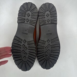 May include: A pair of brown leather boots with black rubber soles. The soles have a deep tread pattern for traction. The size 37 boots are from the Bata brand.