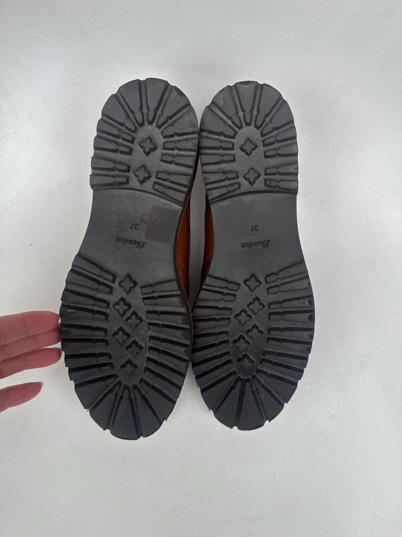 May include: A pair of brown leather boots with black rubber soles. The soles have a deep tread pattern for traction. The size 37 boots are from the Bata brand.