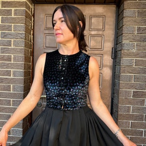 May include: A black sleeveless top with a paisley pattern and a black skirt. The top has a button closure and a belt.